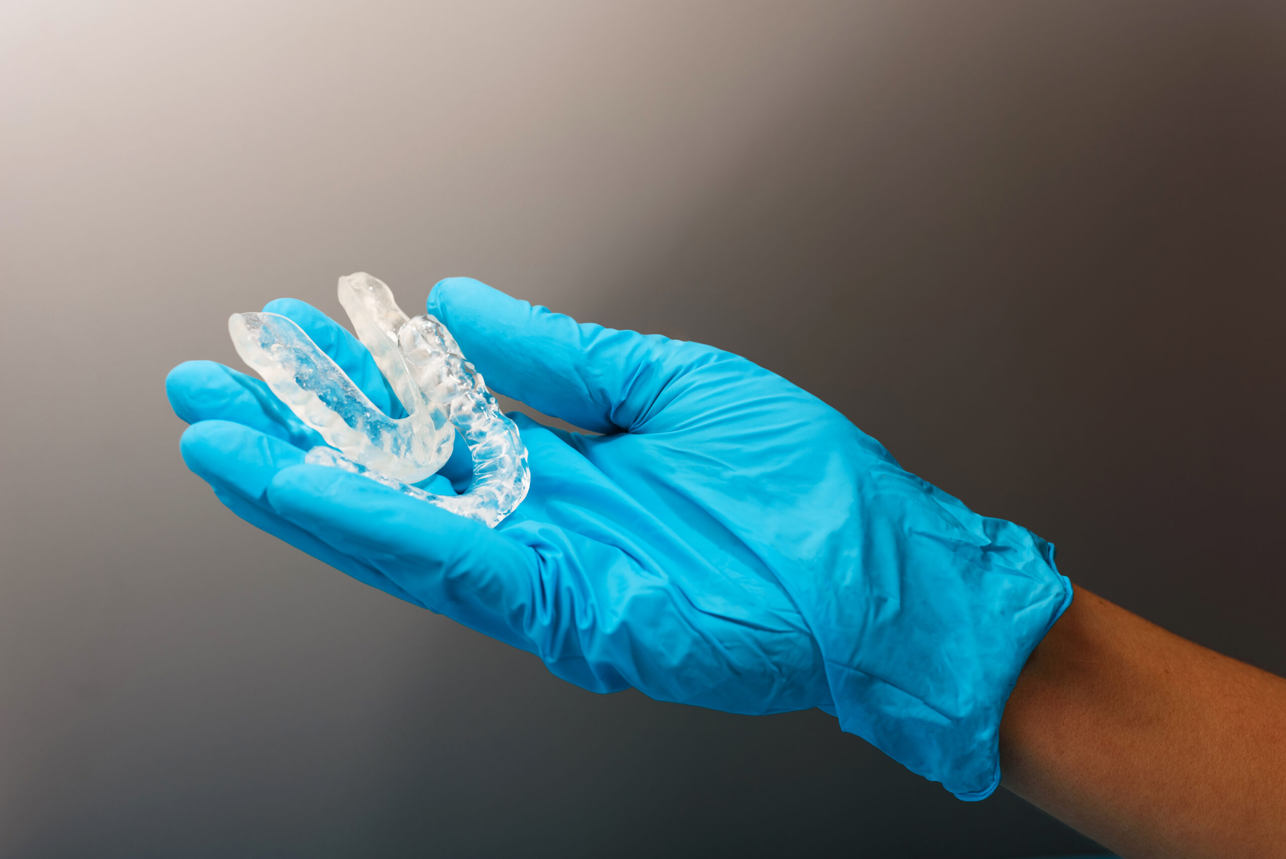 Gloved hand holding clear dental aligners for orthodontic treatment